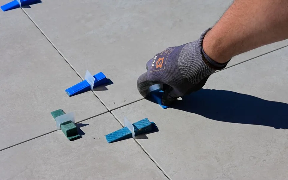 Gloved hand setting levelling spacers between newly laid tiles